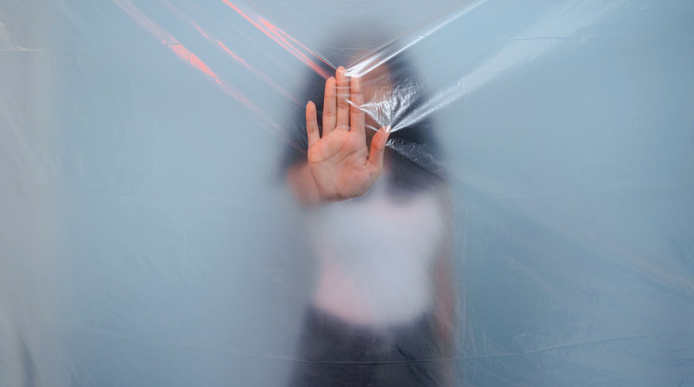 Person hinter transparenter Plastikfolie streckt die Hand aus als Stopp-Geste