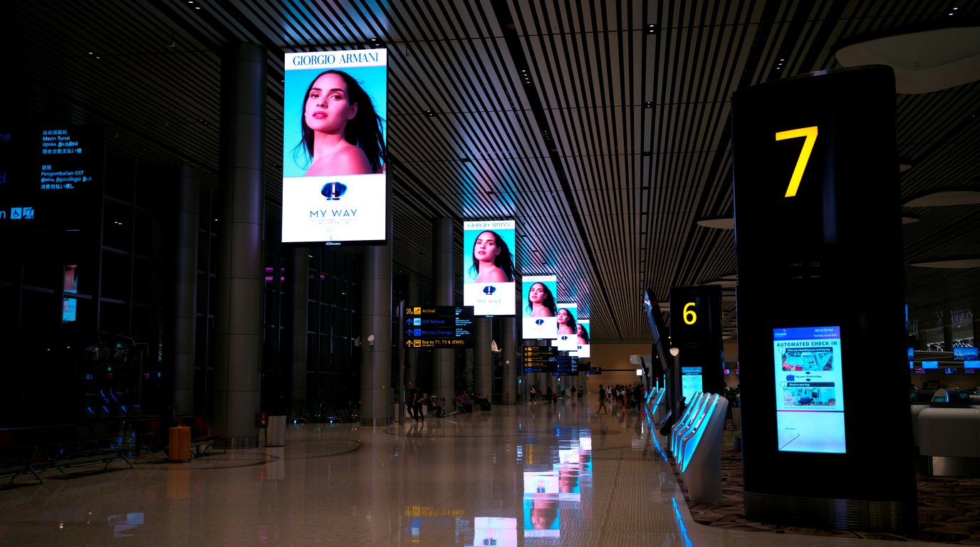 Flughafen-Terminal mit reihenweise digitalen Werbedisplays einer Modemarke, nächtliche Atmosphäre