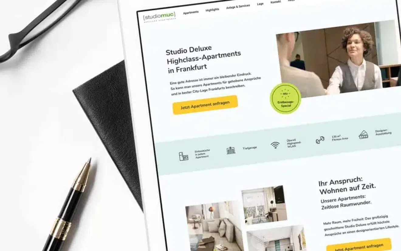 Tablet on a white desk showing the studiomuc serviced apartments website with its booking call to action, next to glasses and a pen