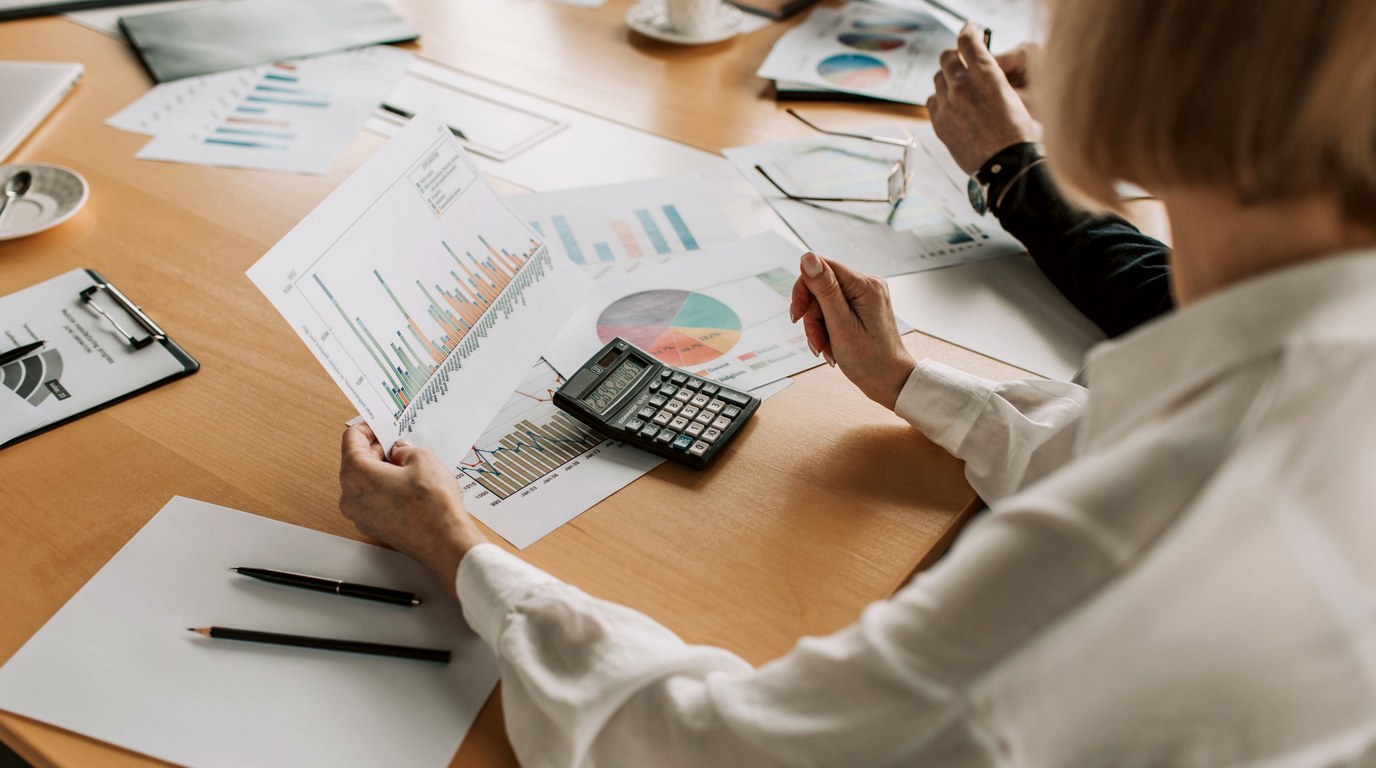 Frau mit Taschenrechner wertet ausgedruckte Finanzdiagramme und Tabellen am Schreibtisch aus