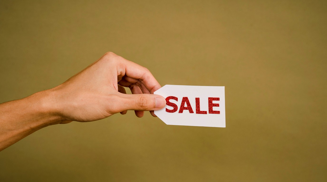 Hand hält kleines weißes Preisschild mit dem Wort Sale in roter Schrift