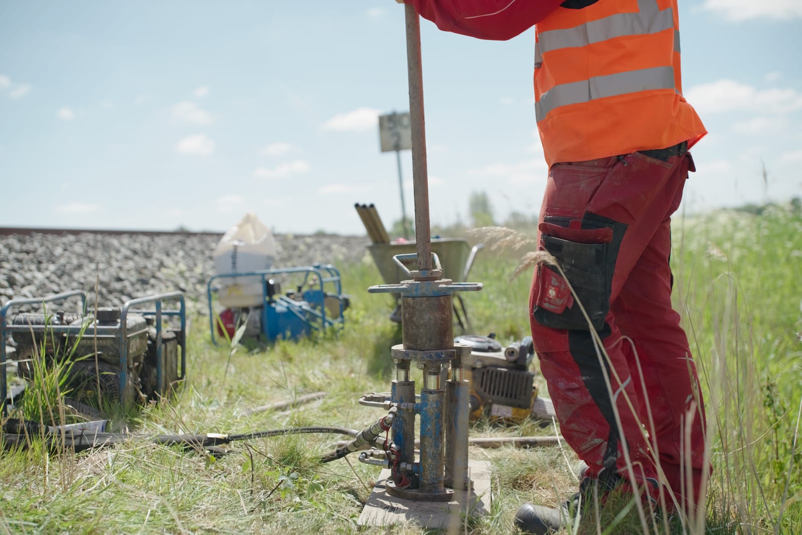 TerraTec-Mitarbeiter in roter Arbeitskleidung bedient ein hydraulisches Bohrgerät neben einer Bahnstrecke