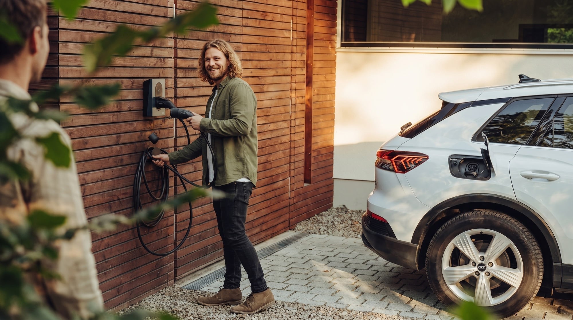 Mann steckt den Ladestecker an seiner privaten Wallbox ein, daneben sein Elektroauto