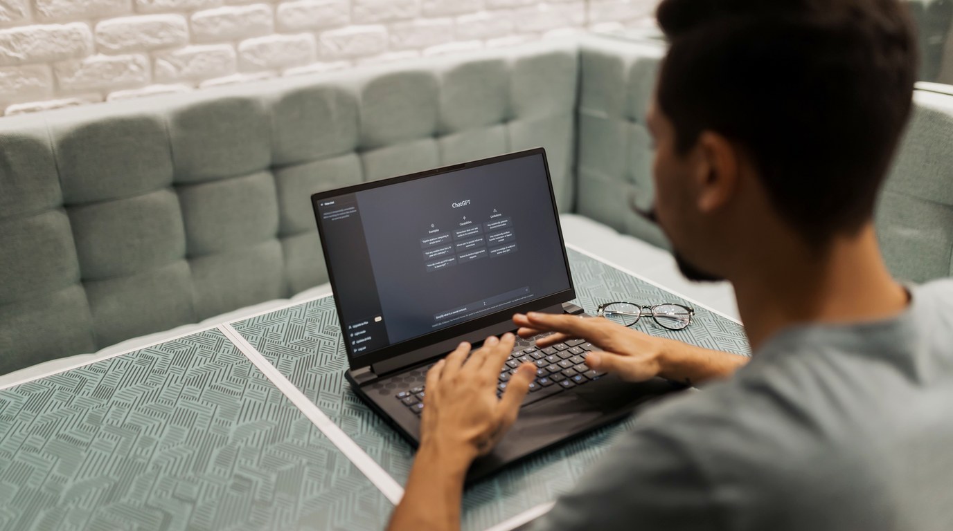 Mann tippt an einem Laptop, auf dessen Bildschirm die ChatGPT-Startseite geöffnet ist
