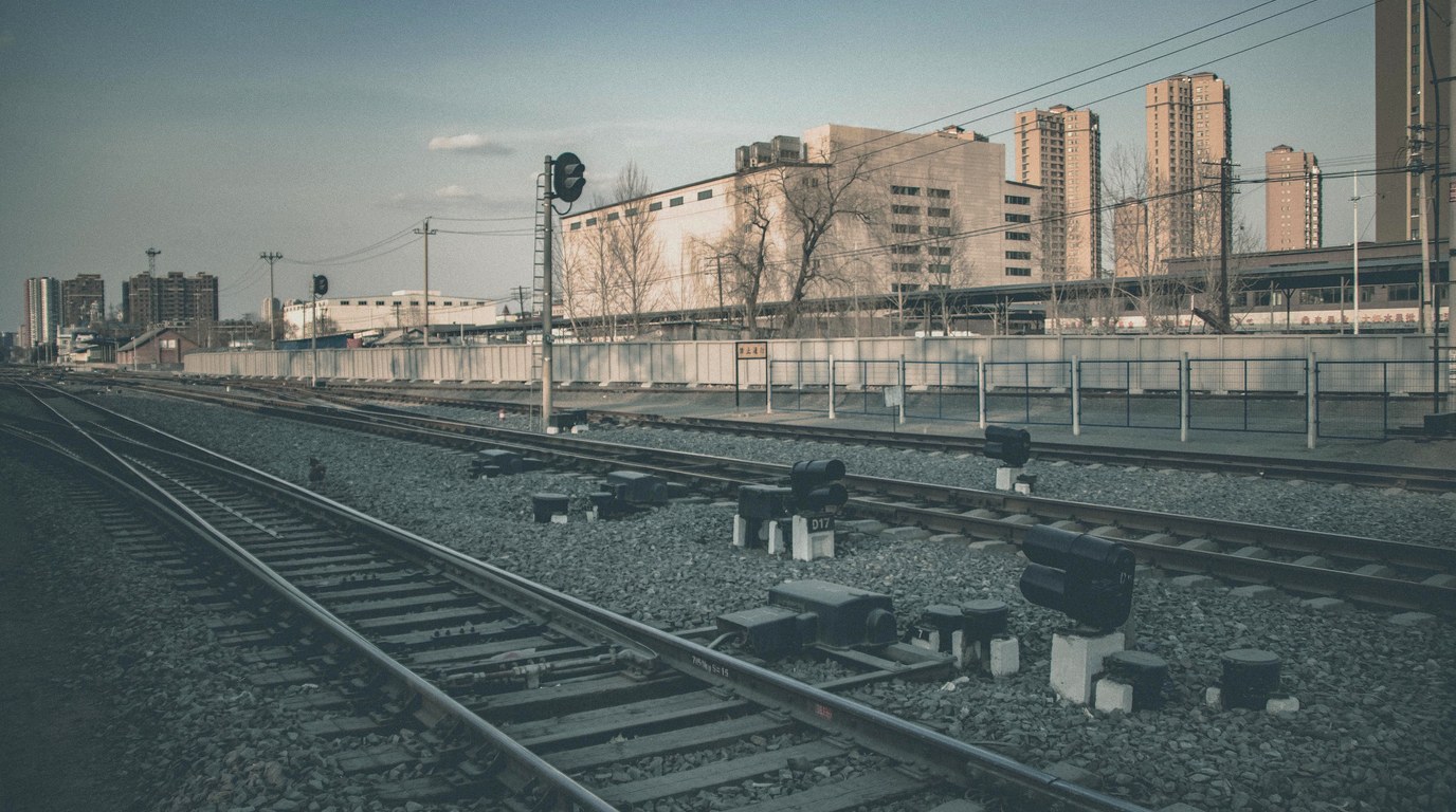 Mehrere Bahngleise mit Weichen und einem Signalmast vor einer Stadtsilhouette im Tageslicht