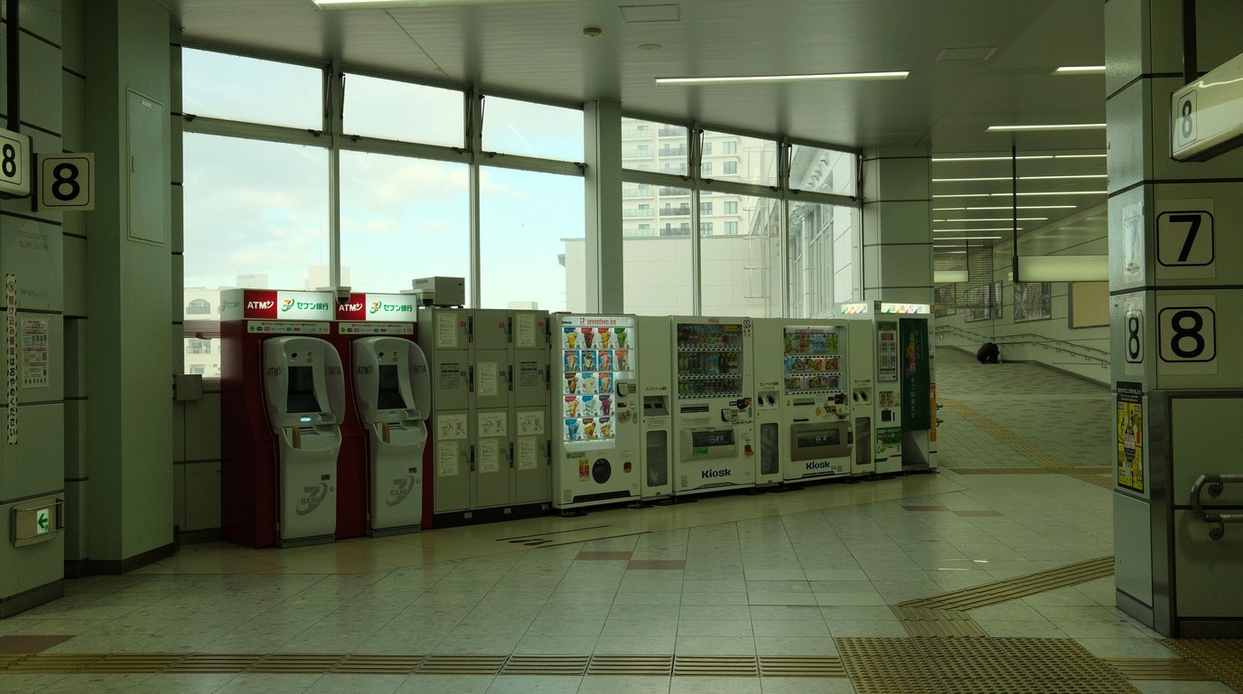 Reihe aus Geldautomaten, Schließfächern und Verkaufsautomaten in einer hellen Bahnhofshalle