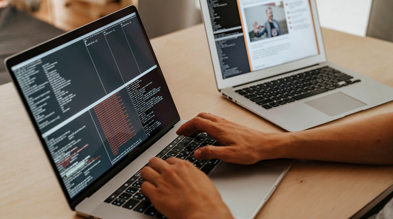 Hände tippen auf einem MacBook mit geöffnetem Terminalfenster, dahinter steht ein zweiter Laptop auf dem Schreibtisch