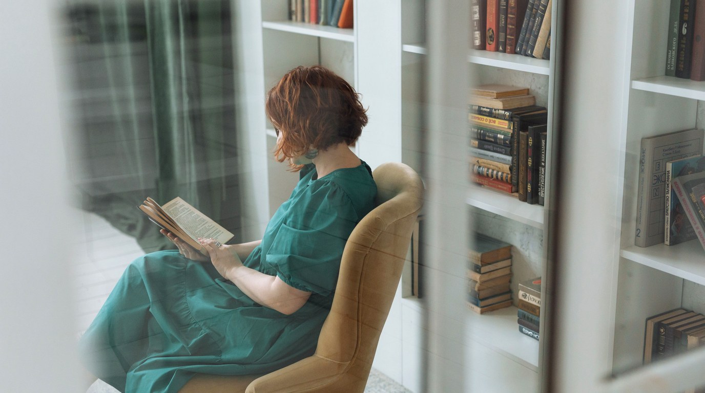 Frau im grünen Kleid liest in einem Sessel vor weißen Bücherregalen